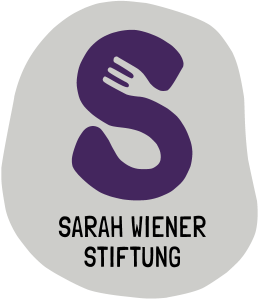 Ein stilisierter violetter Buchstabe „S“ mit einer Gabel in der oberen Kurve, über dem Text „Sarah Wiener Stiftung“ auf grauem, unregelmäßigem Hintergrund.